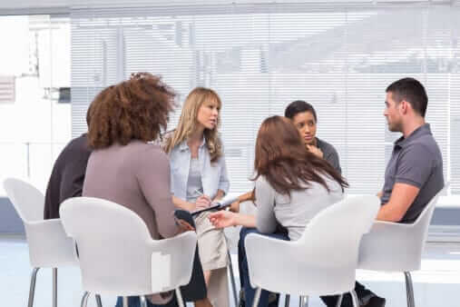 Group of people sitting in a circle during a support group meeting in a modern office setting