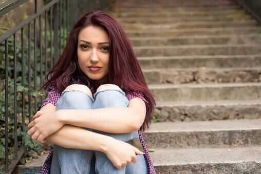 Young woman on steps hugging herself knows first-hand about teen drug abuse.
