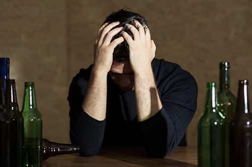 A man with his head in hands wondering the causes of alcoholism