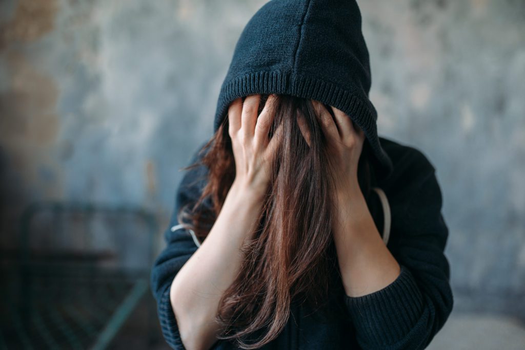 image of a woman in a sweatshirt with her head in her hands struggling with heroin withdrawal.