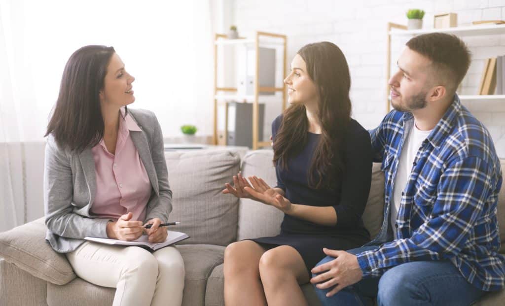 Successful couple therapy. Cheerful young spouses talking to professional marital counselor at office