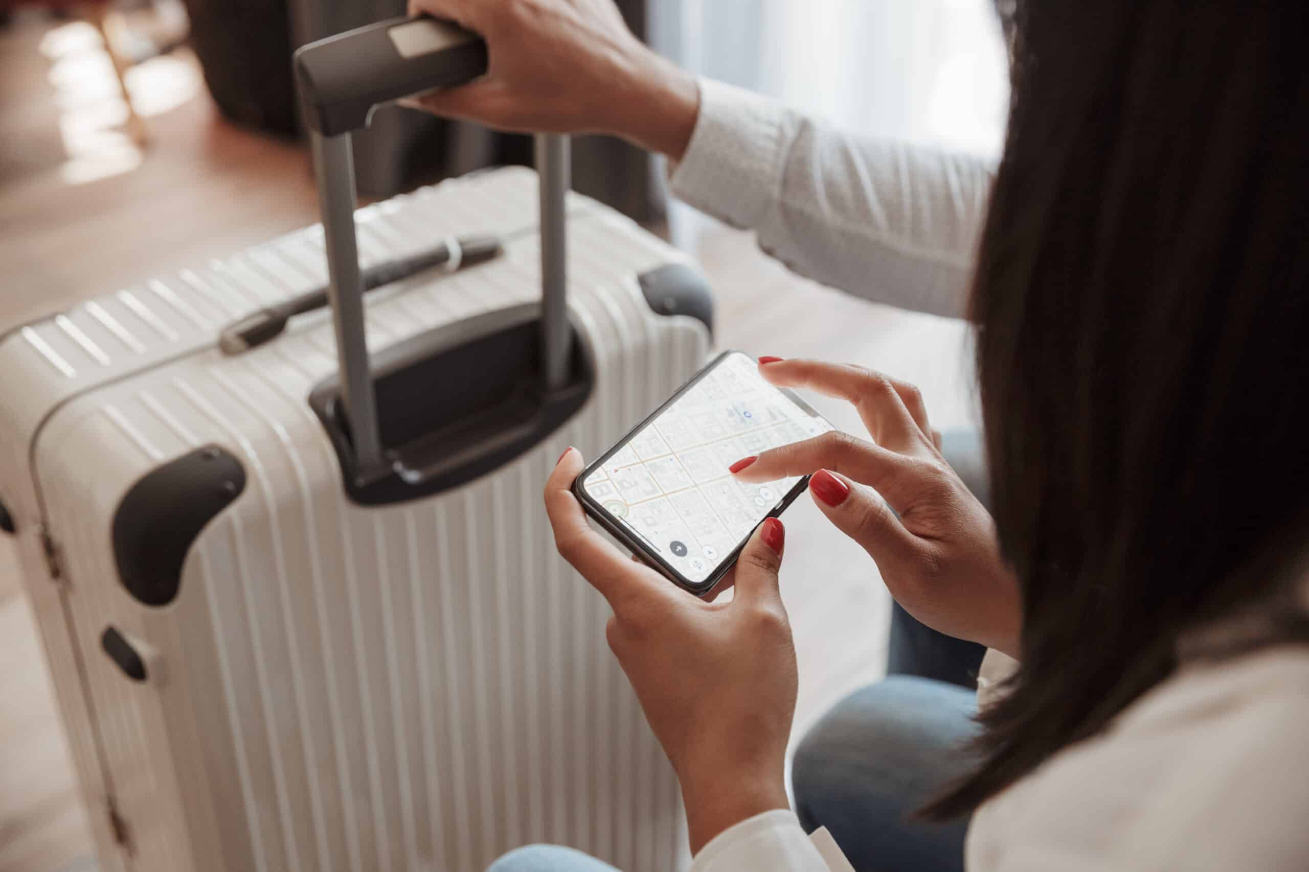 Cropped photo from top of couple with luggage at hotel room, brunette woman holding smartphone and checking location using online map. Holiday or vacation concept