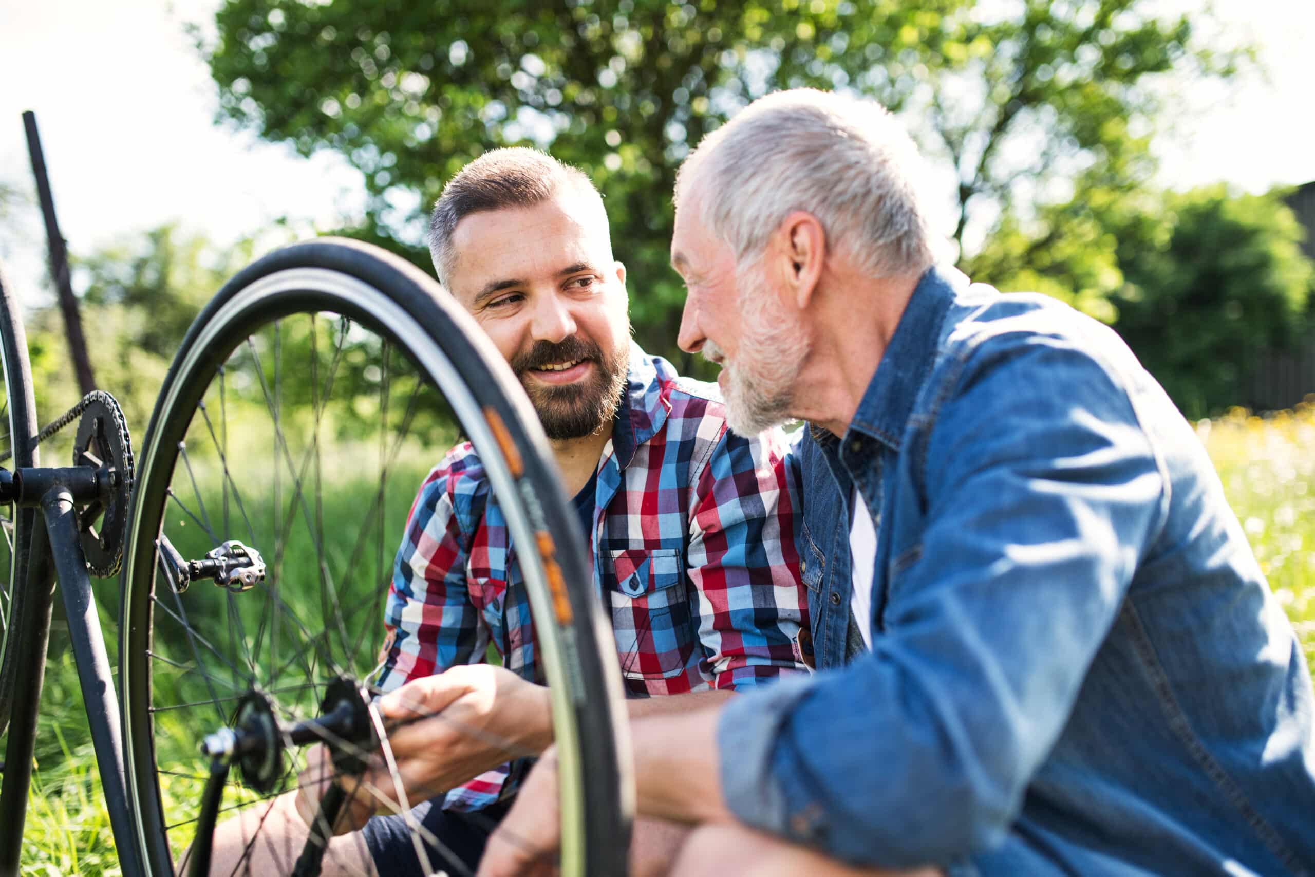 An adult hipster son and senior father repairing bicycle outside on a sunny summer day.