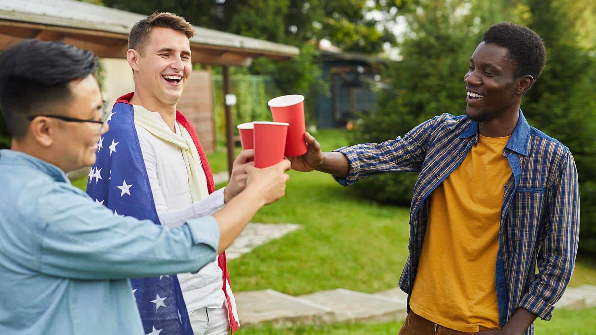 Waist up portrait of multi-ethnic group of men drinking beer while enjoying outdoor party in Summer for Independence day