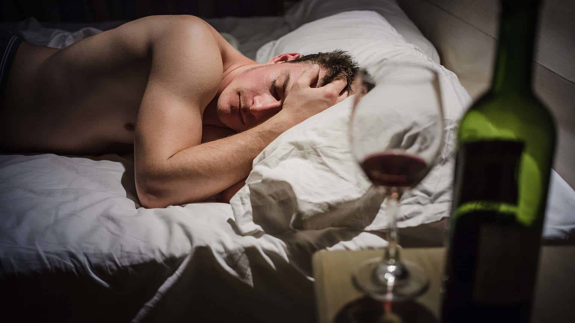 Hangover Man with Headaches in a Bed at Night and Wine bottle