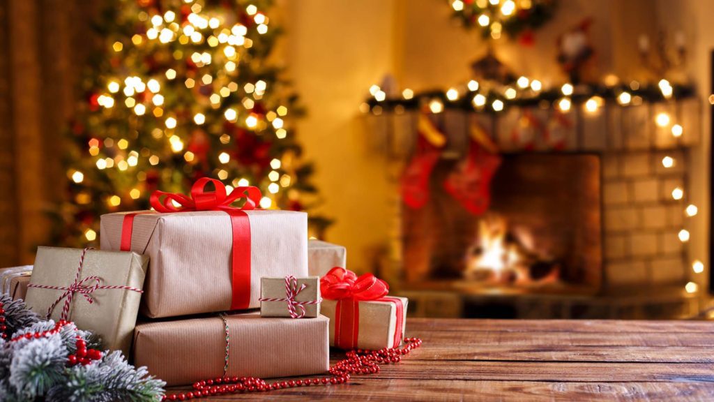 Christmas presents on wooden table decorated fir tree and fire place winter holidays concept