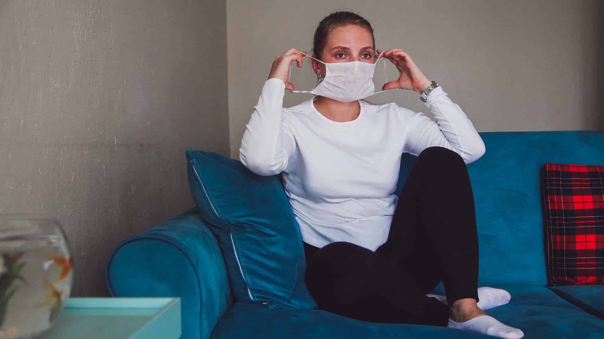 caucasian woman sitting at home with her mask on self isolating
