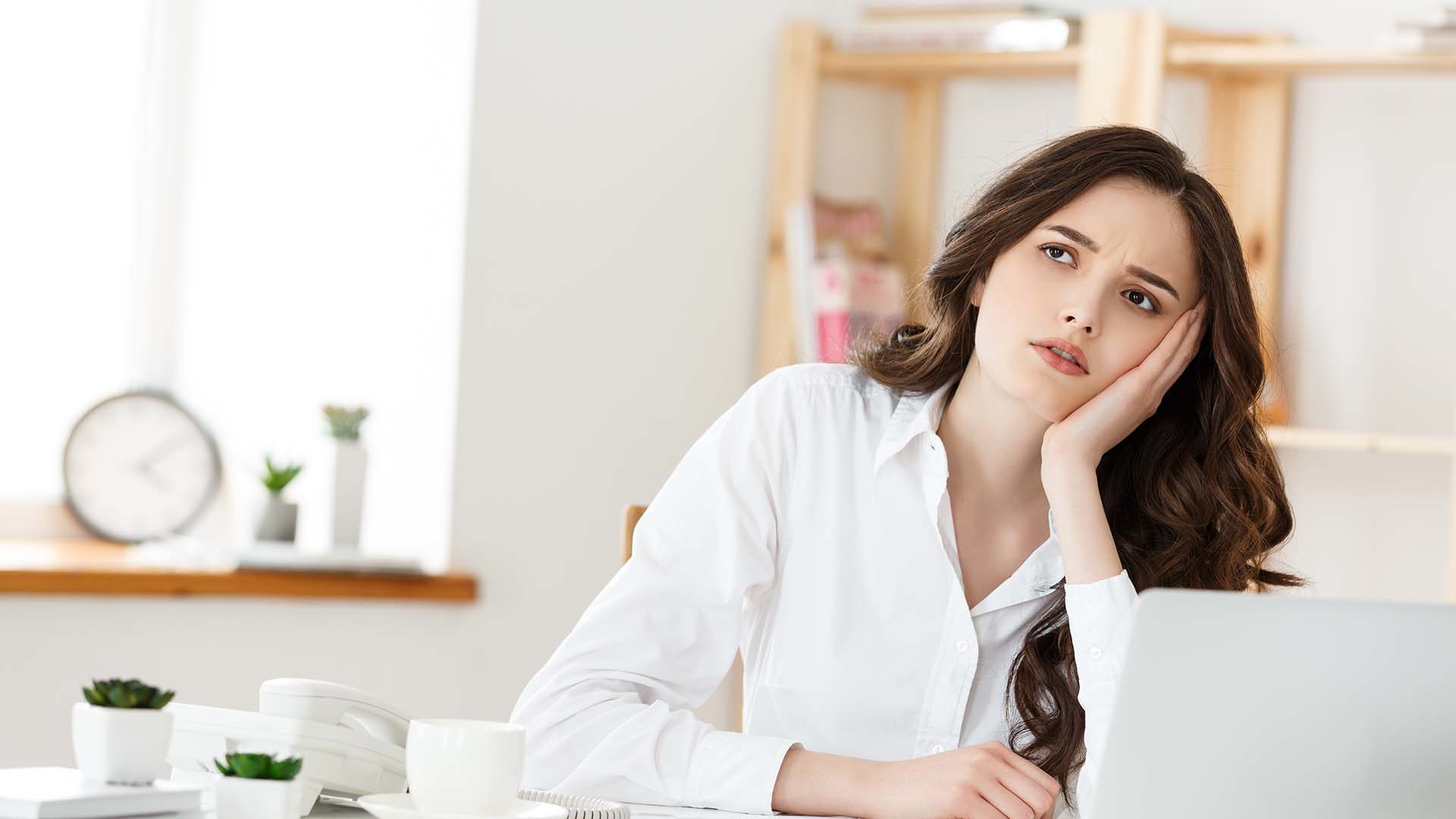 thoughtful woman with hand under chin bored at work, looking away sitting near laptop, demotivated office worker feels lack of inspiration, no motivation.