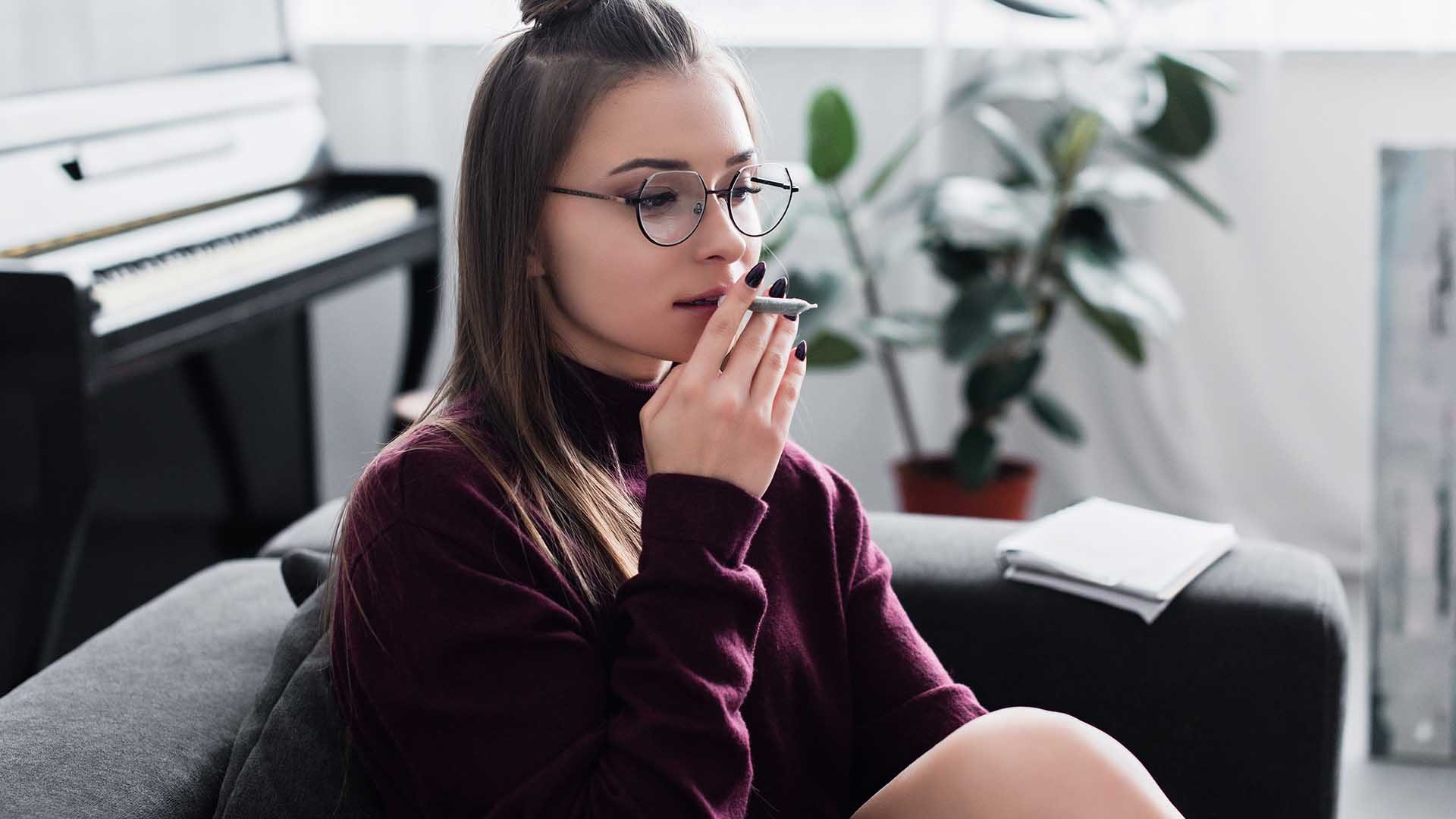 beautiful girl sitting on couch and smoking marijuana joint in living room
