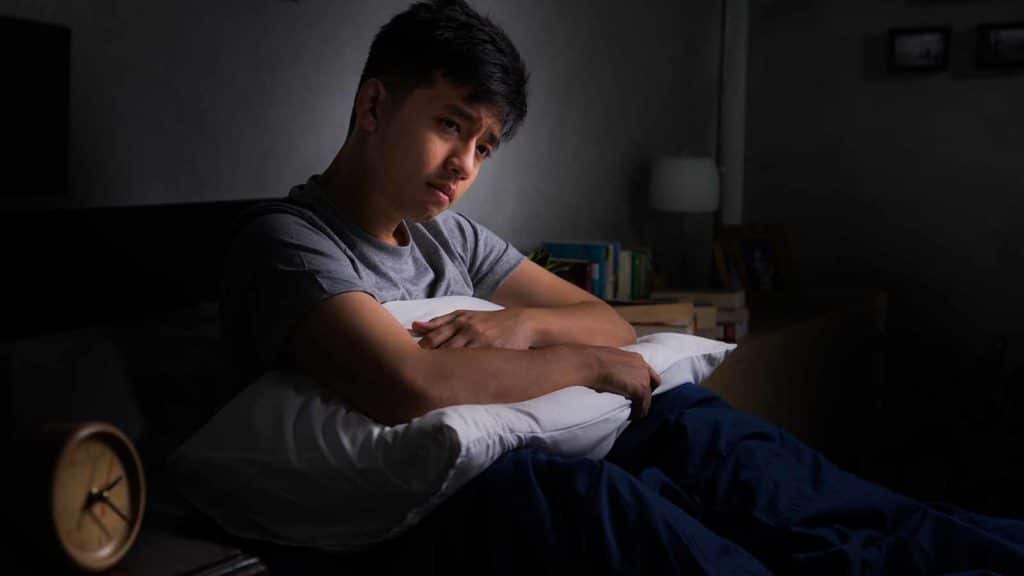 Depressed young man suffering from insomnia sitting in bed