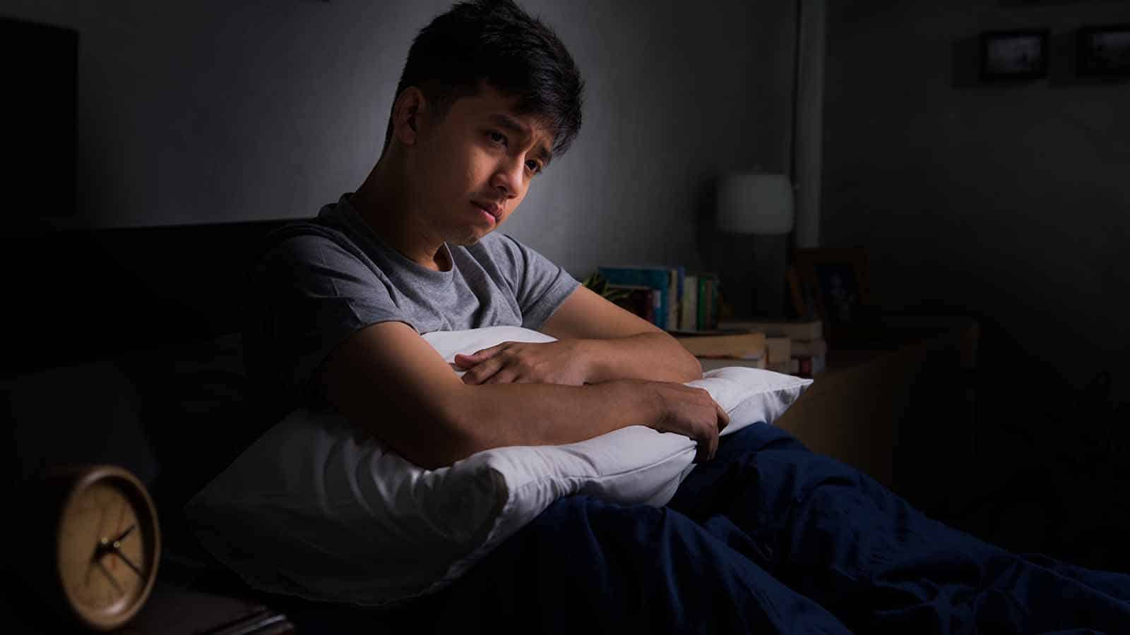 Depressed young man suffering from insomnia sitting in bed